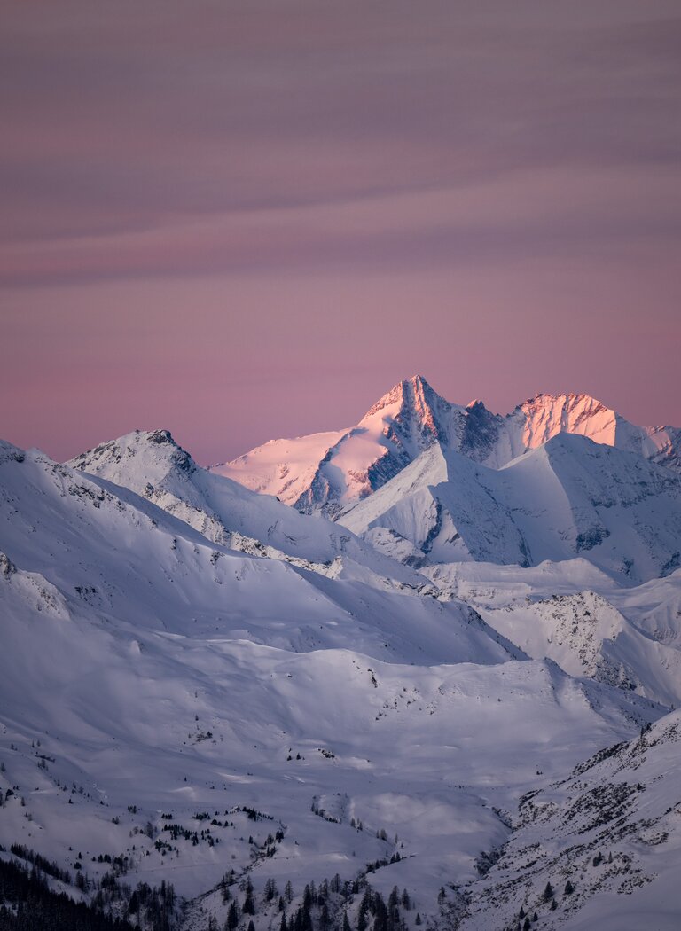 Verschneite Alpen mit rosa Himmel bei Sonnenuntergang, Berggipfel leuchten in warmem Licht. | © Dorfgasteiner Bergbahnen AG