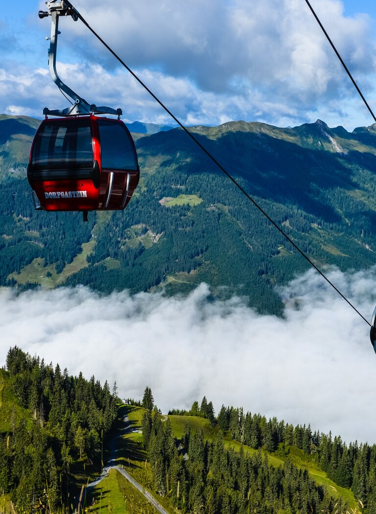 Two cable cars float above a sea of clouds with alpine landscape and small reservoir below. | © Dorfgasteiner Bergbahnen AG