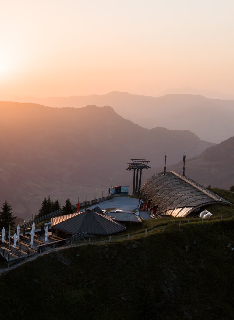 Bergstation mit Terrasse und Speicherteich auf einem Gipfel vor Bergketten im Licht der Abendsonne. | © Dorfgasteiner Bergbahnen AG