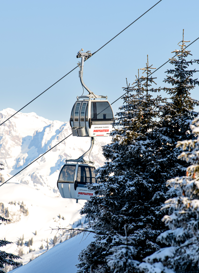 Zwei Gondeln einer Seilbahn fahren zwischen schneebedeckten Bäumen vor Bergkulisse bei klarem Winterhimmel | © Dorfgasteiner Bergbahnen AG