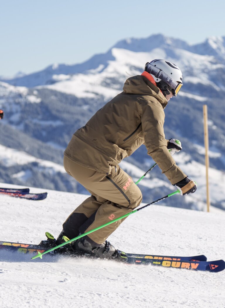 Two skiers descend a groomed slope with snow-covered mountains beneath a clear winter sky. | © Dorfgasteiner Bergbahnen AG