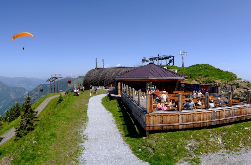 Panorama mit Paragleitern, Bergstation und Sonnenterrasse im Sommer in Großarl | © Grossarler Bergbahnen GmbH & Co KG Paragleiter über dem Großarltal bei Bergstation mit Ausflugsgästen auf Sonnenterrasse und Panoramablick | © Grossarler Bergbahnen GmbH & Co KG