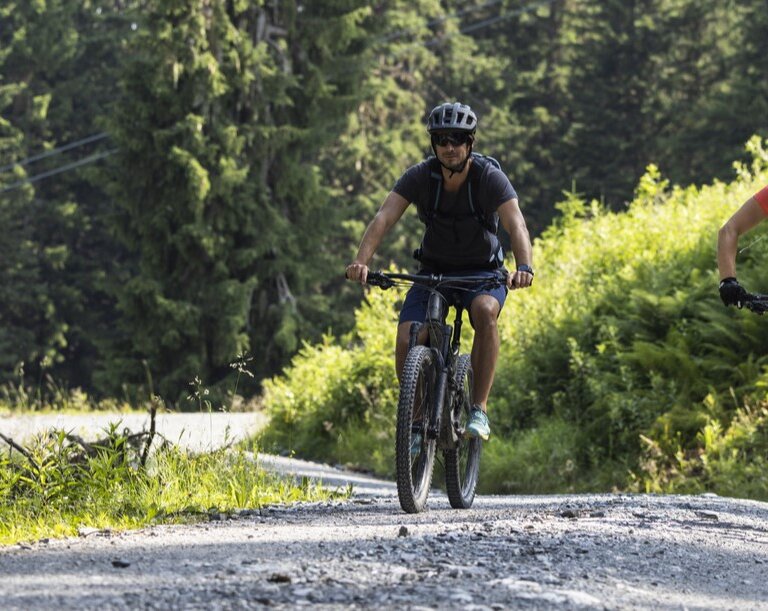 Zwei Mountainbiker fahren auf einem sonnigen Schotterweg durch die grüne Waldlandschaft im Gasteinertal. | © Gasteiner Bergbahnen AG