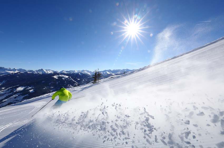 Skier in bright jacket rides through fresh powder snow in sunshine with wide alpine view. | © Tourismusverband Großarltal