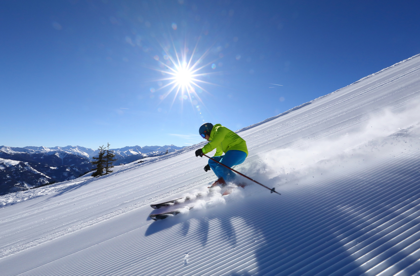 Skier in green jacket carving through powder on a freshly groomed slope in bright sunshine. | © Tourismusverband Großarltal