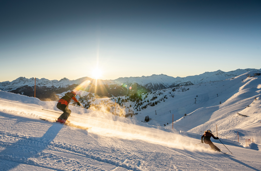 Two winter sports enthusiasts ski at sunrise on freshly groomed slope in Großarltal with mountain view. | © Tourismusverband Großarltal