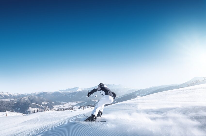 Skifahrer fährt ruhig auf breiter, präparierter Piste mit Blick auf das verschneite Alpenpanorama. | © Ski amadé GmbH